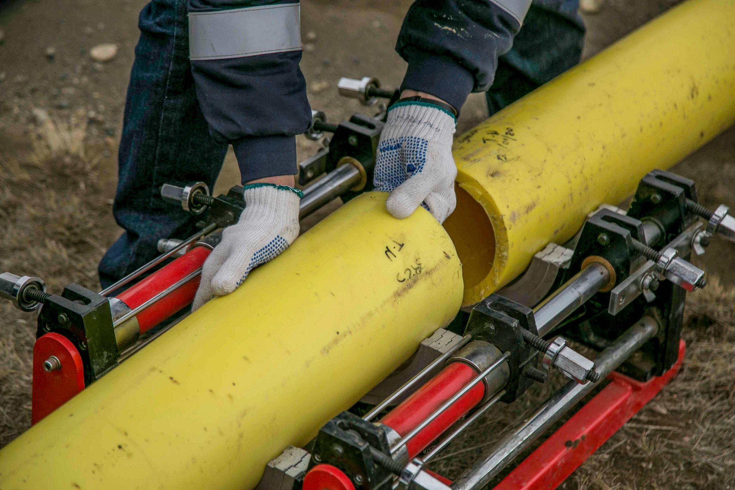 Close-up view of a worker using equipment to install yellow pipes outdoors, focusing on hands and tools.